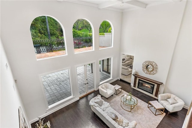 living area featuring dark wood-style floors, a high ceiling, a glass covered fireplace, and beamed ceiling