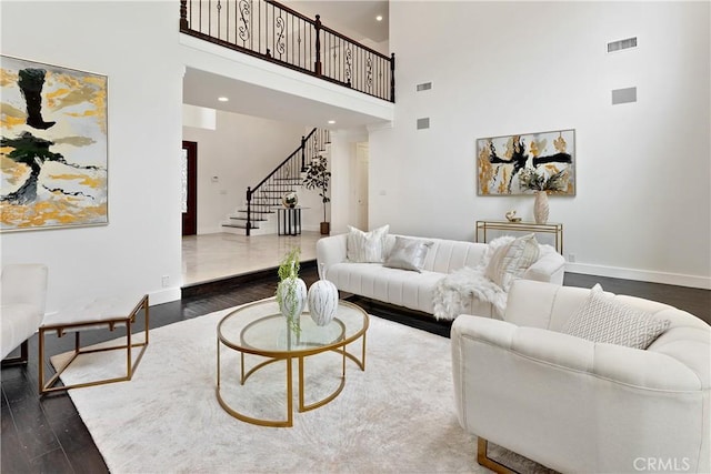 living area featuring stairway, a towering ceiling, dark wood-style floors, visible vents, and baseboards