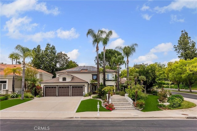 mediterranean / spanish-style house with a tiled roof, driveway, an attached garage, roof mounted solar panels, and stucco siding