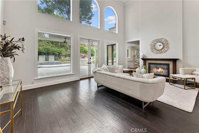 living room featuring a high ceiling, ornamental molding, baseboards, a glass covered fireplace, and hardwood / wood-style flooring