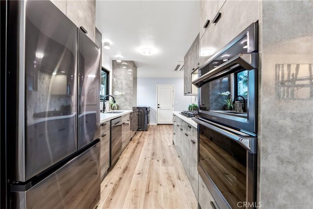 kitchen with a sink, light wood-style floors, light countertops, appliances with stainless steel finishes, and modern cabinets