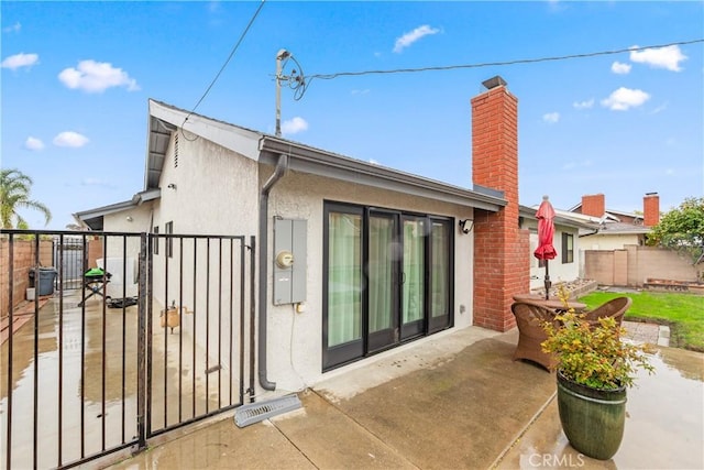 rear view of house featuring a patio, fence, a gate, stucco siding, and a chimney