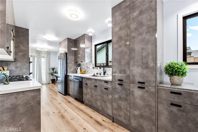 kitchen featuring black cooktop, light wood-style floors, freestanding refrigerator, a sink, and dishwasher