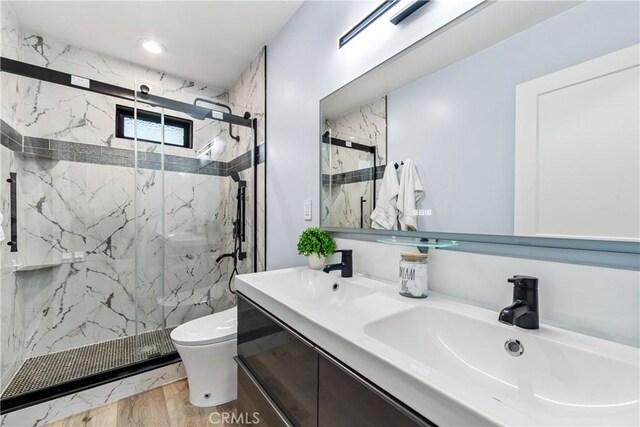 full bath with toilet, double vanity, a marble finish shower, and a sink