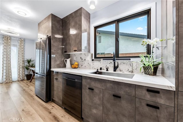 kitchen with dark brown cabinetry, a sink, light wood-type flooring, freestanding refrigerator, and dishwasher