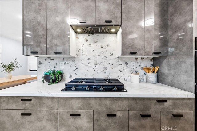 kitchen featuring gas stovetop, light stone counters, ventilation hood, and decorative backsplash