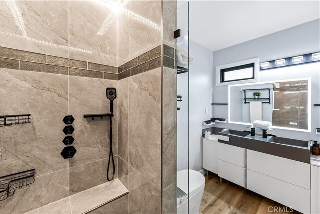 bathroom with toilet, tiled shower, wood finished floors, and vanity