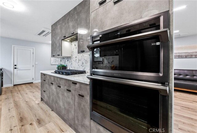 kitchen with black gas stovetop, stainless steel double oven, visible vents, light wood finished floors, and tasteful backsplash