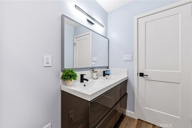 bathroom featuring wood finished floors, a sink, baseboards, and double vanity