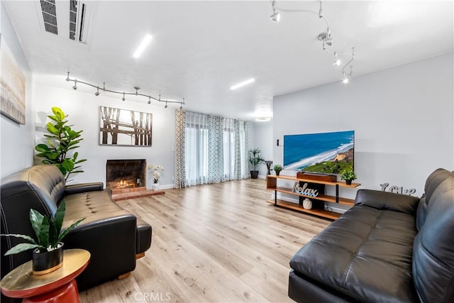 living room featuring visible vents, track lighting, wood finished floors, a warm lit fireplace, and baseboards