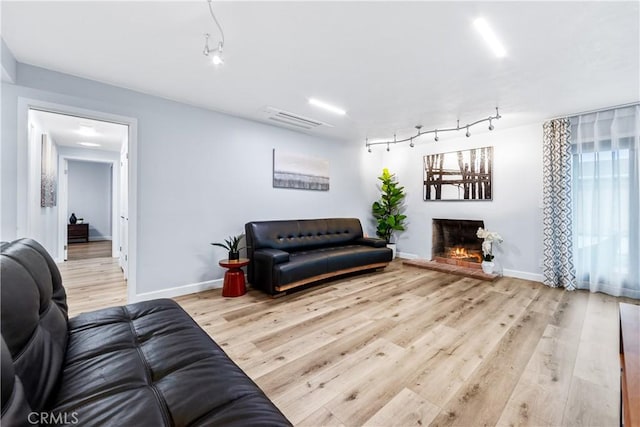 living area with a warm lit fireplace, track lighting, visible vents, and wood finished floors