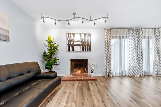 interior space with a lit fireplace, wood finished floors, rail lighting, and baseboards