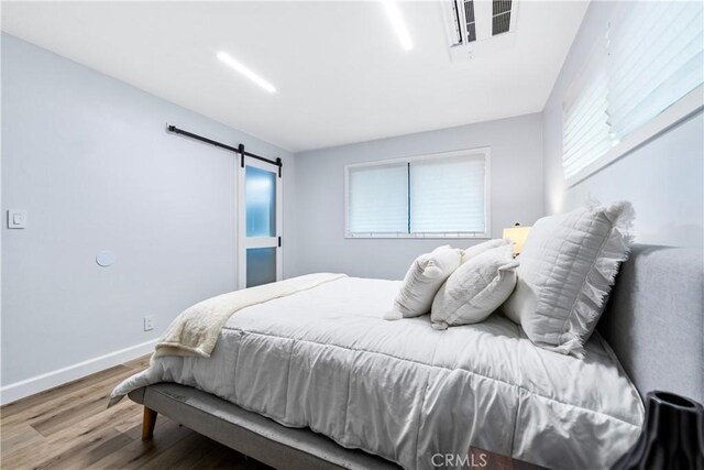 bedroom featuring baseboards, a barn door, visible vents, and wood finished floors