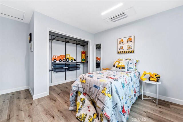 bedroom with baseboards, attic access, visible vents, and wood finished floors