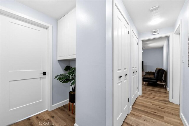 corridor with baseboards, visible vents, and light wood-style floors