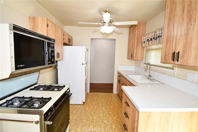 kitchen featuring black microwave, a sink, light countertops, freestanding refrigerator, and gas range oven