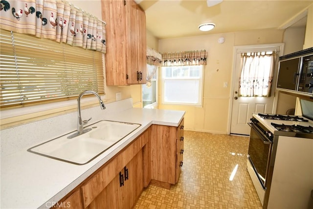 kitchen featuring light countertops, white gas range oven, a sink, and brown cabinets