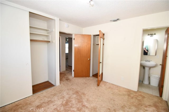 unfurnished bedroom featuring a sink, carpet flooring, visible vents, and connected bathroom