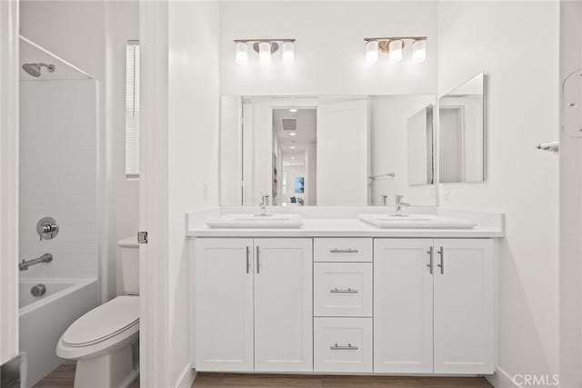 bathroom featuring toilet, double vanity, tub / shower combination, and a sink