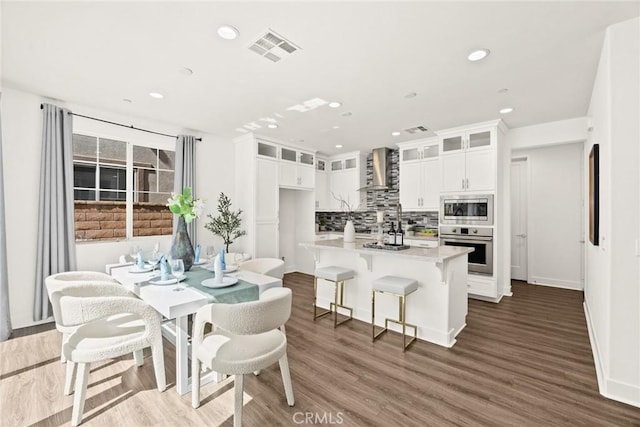 kitchen featuring stainless steel appliances, visible vents, white cabinets, wall chimney range hood, and tasteful backsplash