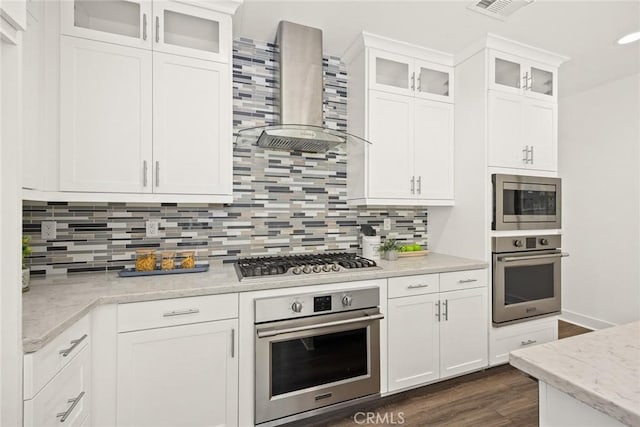 kitchen featuring dark wood-style flooring, stainless steel appliances, tasteful backsplash, white cabinetry, and wall chimney exhaust hood