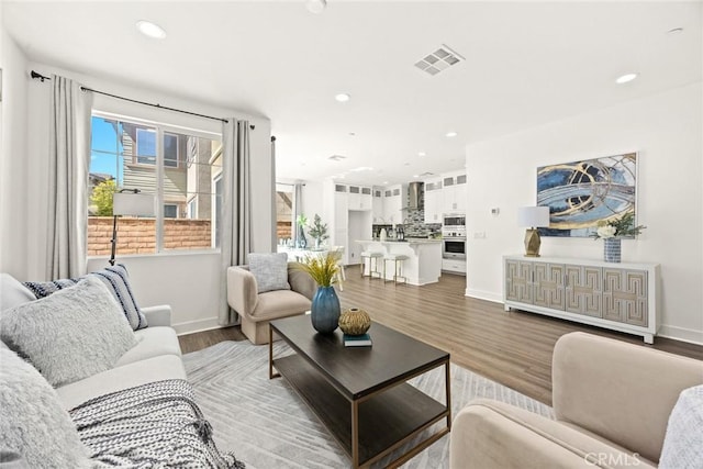 living room with baseboards, visible vents, wood finished floors, and recessed lighting