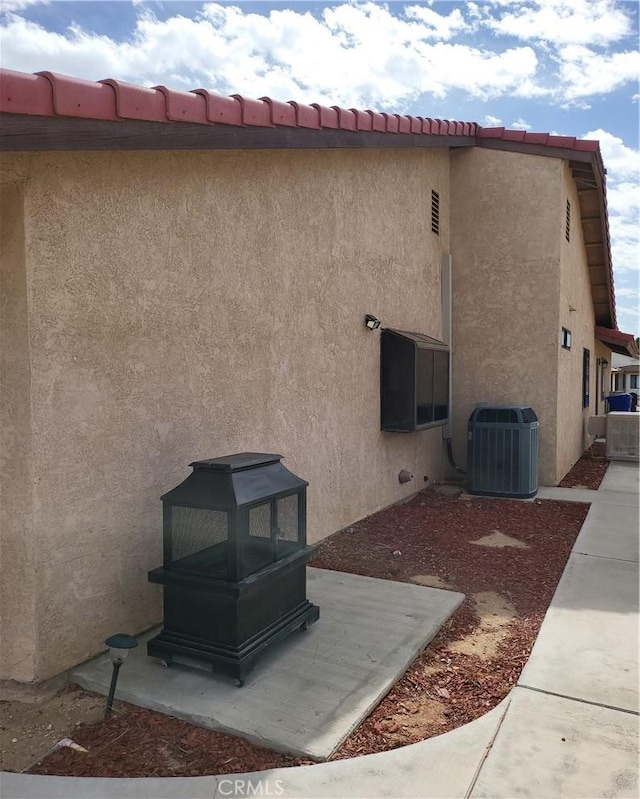 view of property exterior featuring a tile roof, central AC, and stucco siding