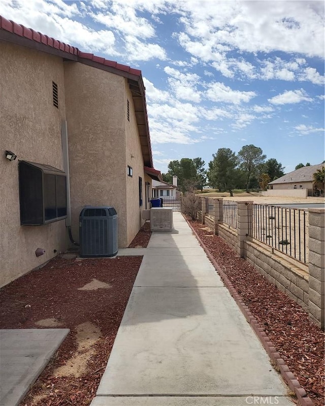 view of side of home with fence, central AC, and stucco siding