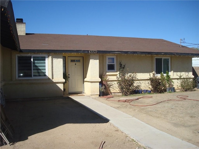 entrance to property featuring a shingled roof, a chimney, and stucco siding