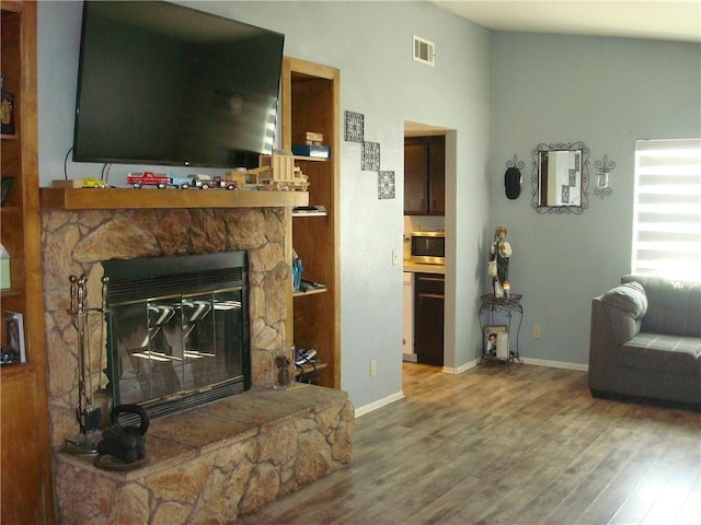 living area with lofted ceiling, wood finished floors, visible vents, and baseboards