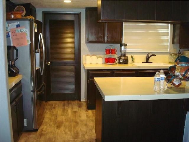 kitchen featuring dark brown cabinetry, a sink, light wood-style floors, light countertops, and stainless steel refrigerator with ice dispenser