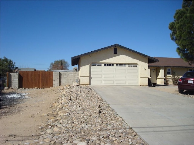 view of front of property featuring a garage, driveway, fence, and stucco siding