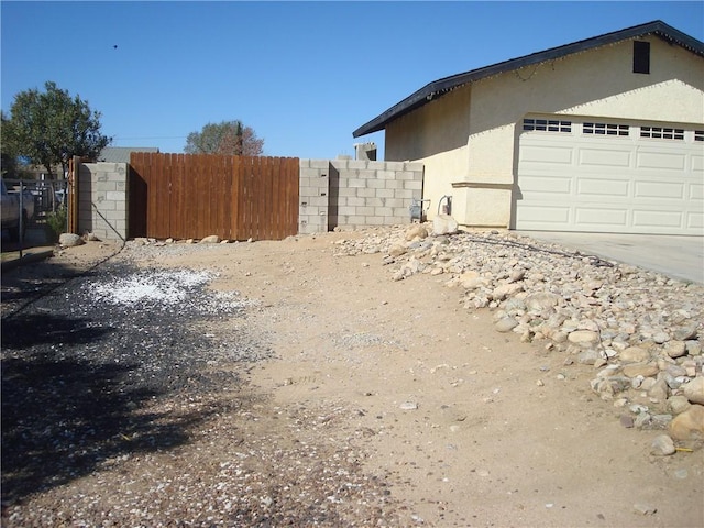 view of side of property with concrete driveway, fence, and stucco siding