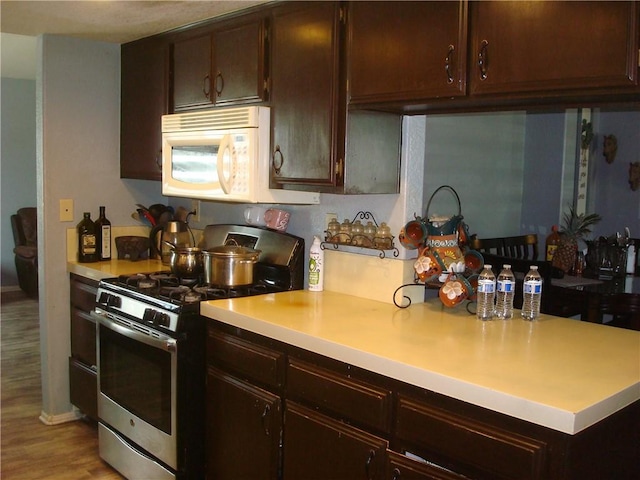 kitchen with stainless steel gas range, dark brown cabinets, white microwave, and light countertops