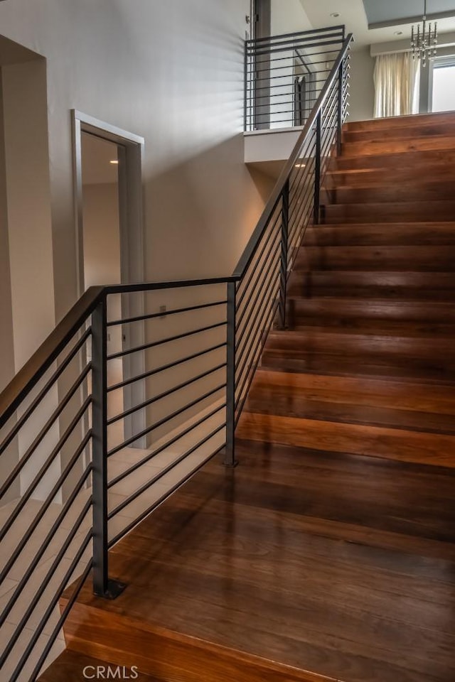 staircase featuring wood finished floors and an inviting chandelier