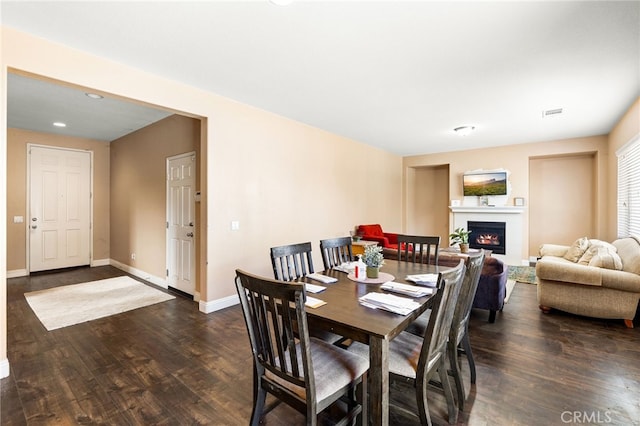 dining space featuring a lit fireplace, baseboards, and wood finished floors