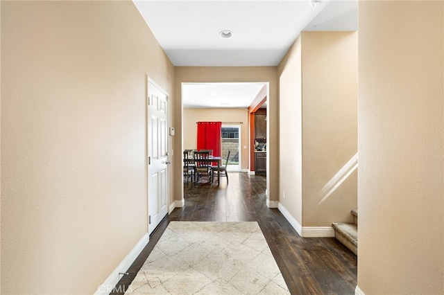 hallway with dark wood-style flooring, baseboards, and stairs