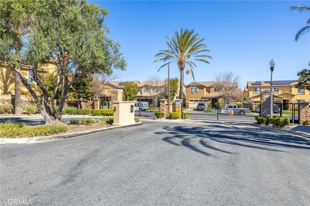 view of street featuring street lights, a gated entry, curbs, a gate, and a residential view