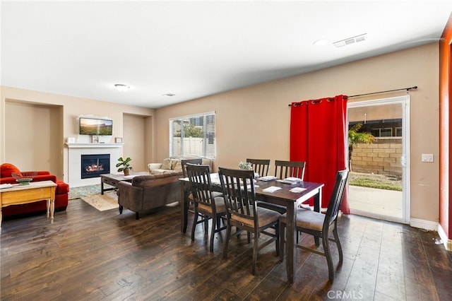 dining room with dark wood-type flooring, visible vents, a lit fireplace, and baseboards