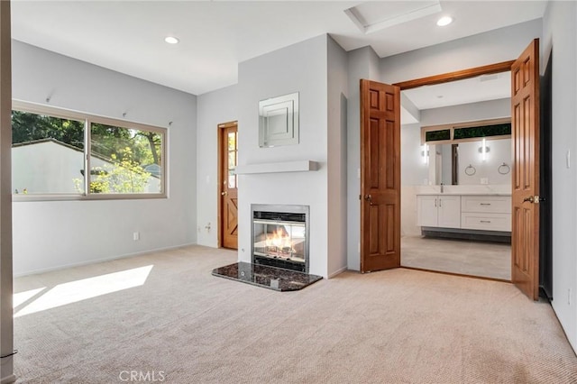 unfurnished living room featuring a glass covered fireplace, baseboards, recessed lighting, and light colored carpet