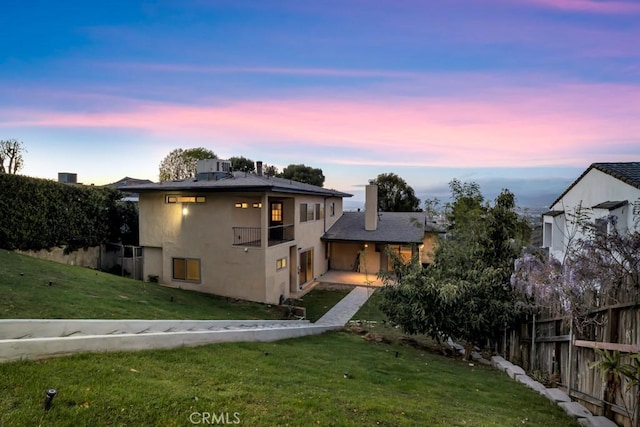 exterior space featuring fence, stucco siding, a lawn, and a balcony