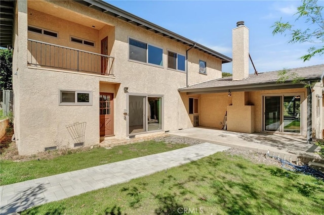 back of house with a lawn, stucco siding, a balcony, and a chimney