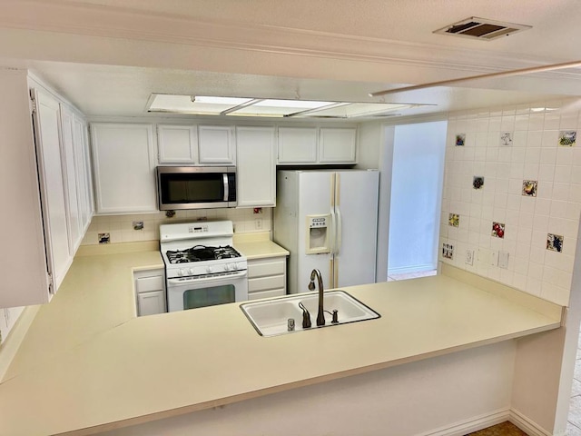 kitchen featuring a peninsula, white appliances, visible vents, and a sink