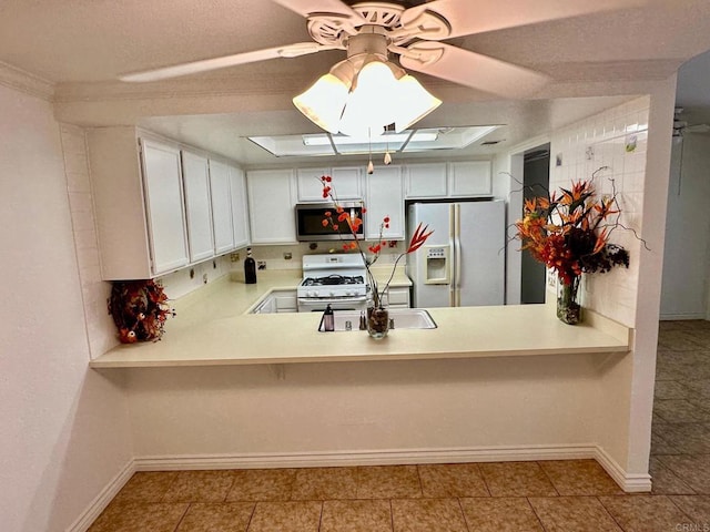 kitchen with baseboards, light countertops, a peninsula, white appliances, and a ceiling fan