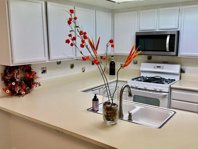 kitchen with white range with gas cooktop, stainless steel microwave, white cabinets, light countertops, and decorative backsplash