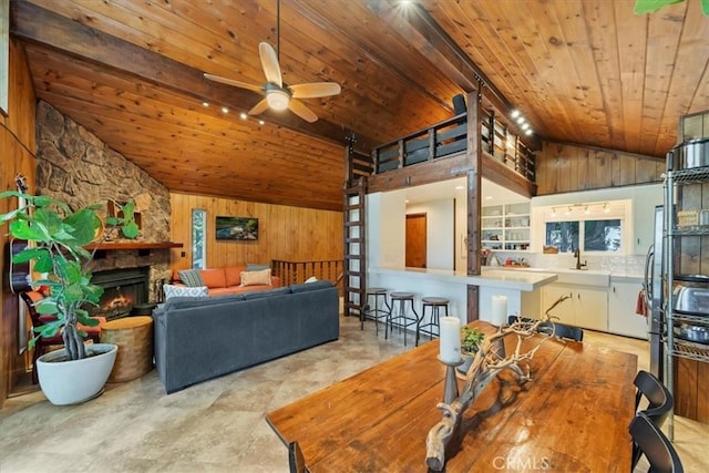 interior space featuring a ceiling fan, lofted ceiling, wood ceiling, wood walls, and a fireplace