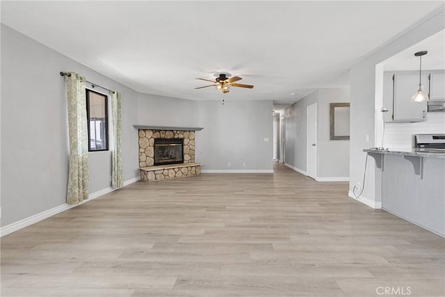 unfurnished living room with light wood-type flooring, baseboards, a ceiling fan, and a stone fireplace