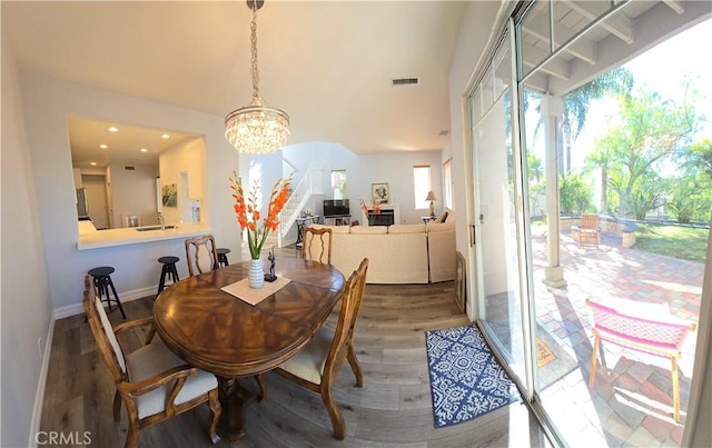 dining area featuring a notable chandelier, wood finished floors, visible vents, baseboards, and stairway