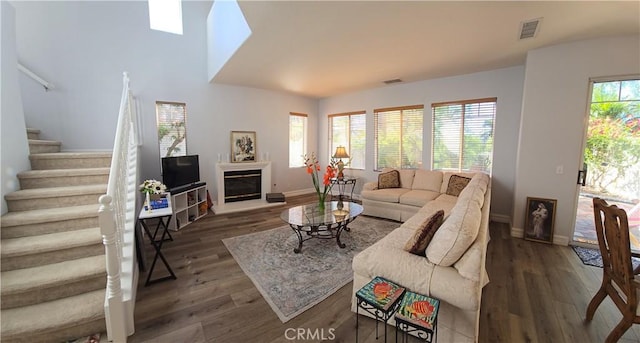 living area featuring baseboards, visible vents, a glass covered fireplace, wood finished floors, and stairs