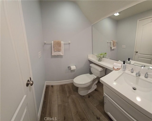 half bath with vanity, wood finished floors, toilet, and baseboards